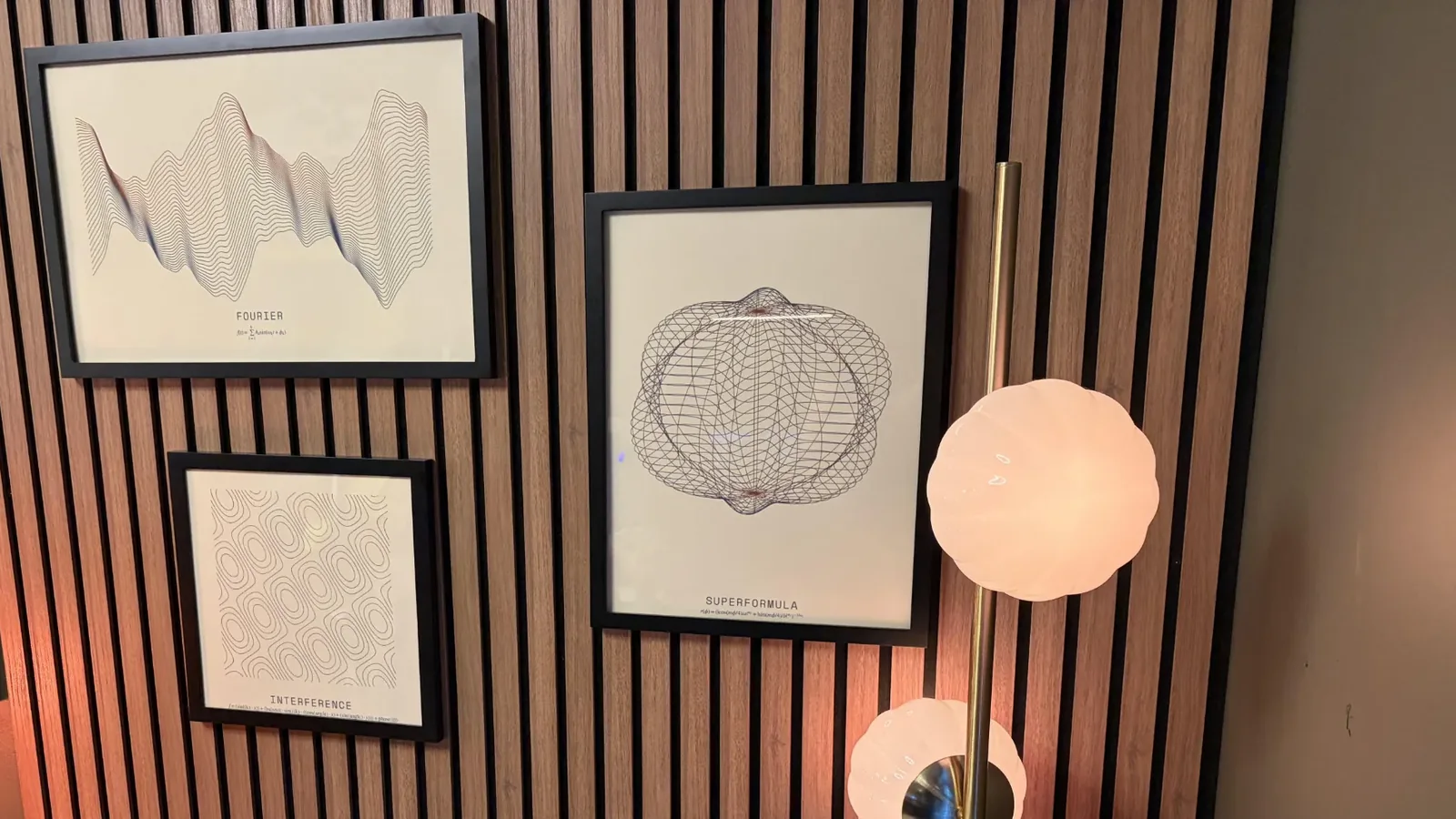 Three framed FORM prints, Fourier, Interference, and Superformula, on a walnut slat wall in my office beside a brass floor lamp