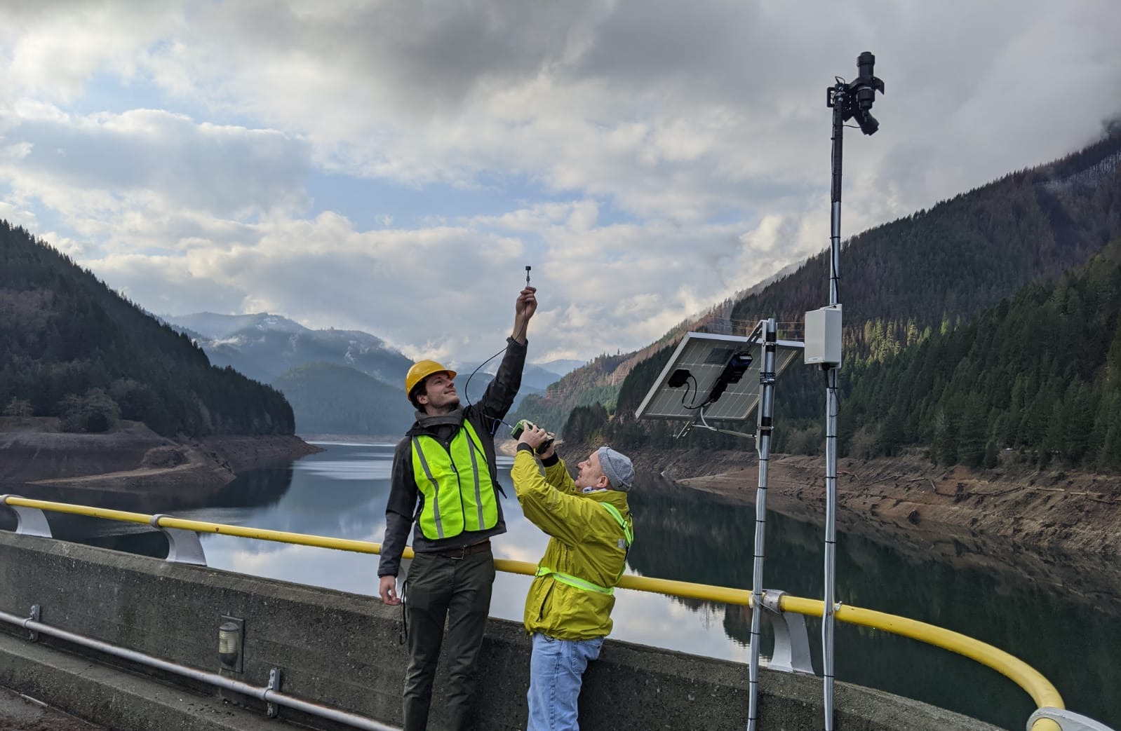 Two field workers beside a mounted sensor and solar panel at Detroit Lake